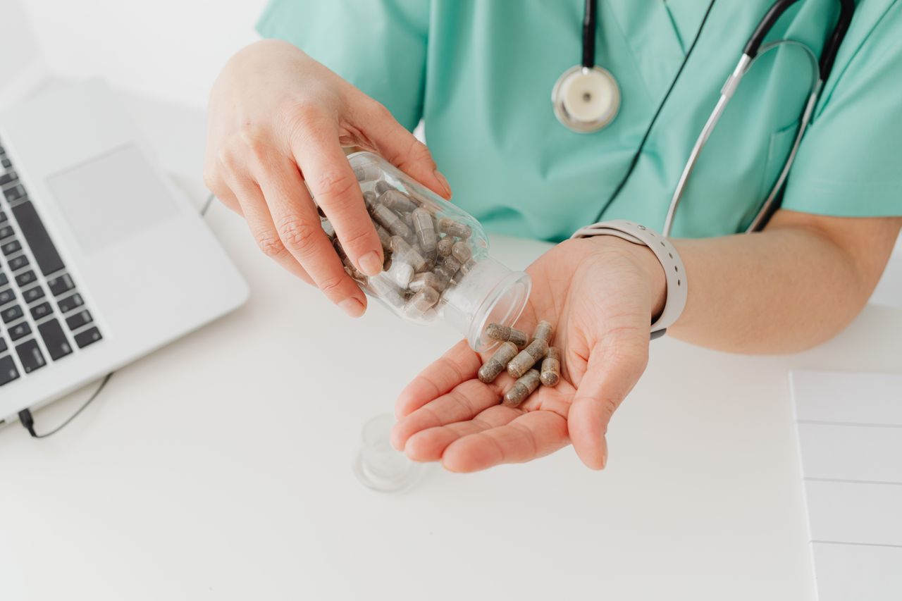 Doctor pouring capsules into hands while wearing a green uniform near a laptop.
